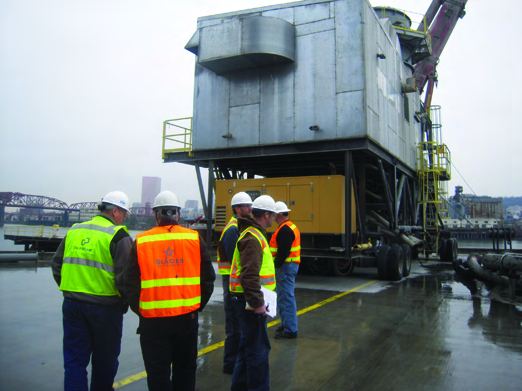 Four workers in hard hats and high-visibility vests inspecting outdoor plant equipment