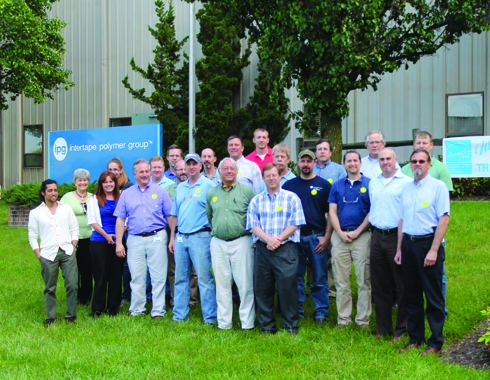 Group photograph of Energy Treasure Hunt participants standing on a lawn in front of an Intertape Polymer Group building