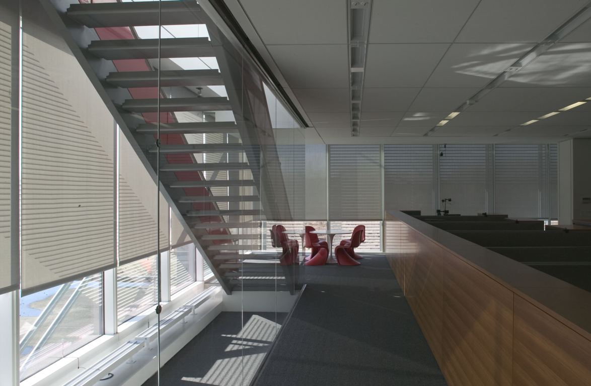 Photograph of the full-size mock-up of the New York Times Building office spaces, showing roller shades, an open stair and red chairs beside a glazed wall.