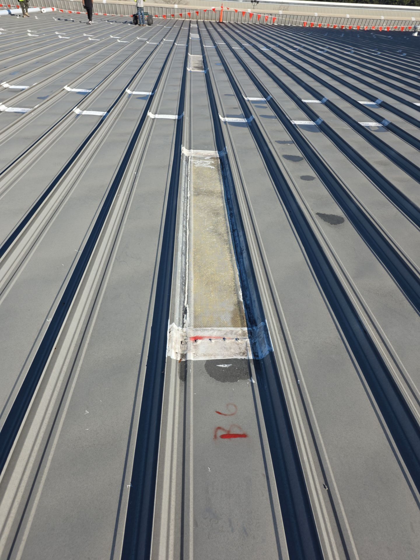 Before photo - Aging standing seam metal roof with existing flush-mounted skylights and weathered condition